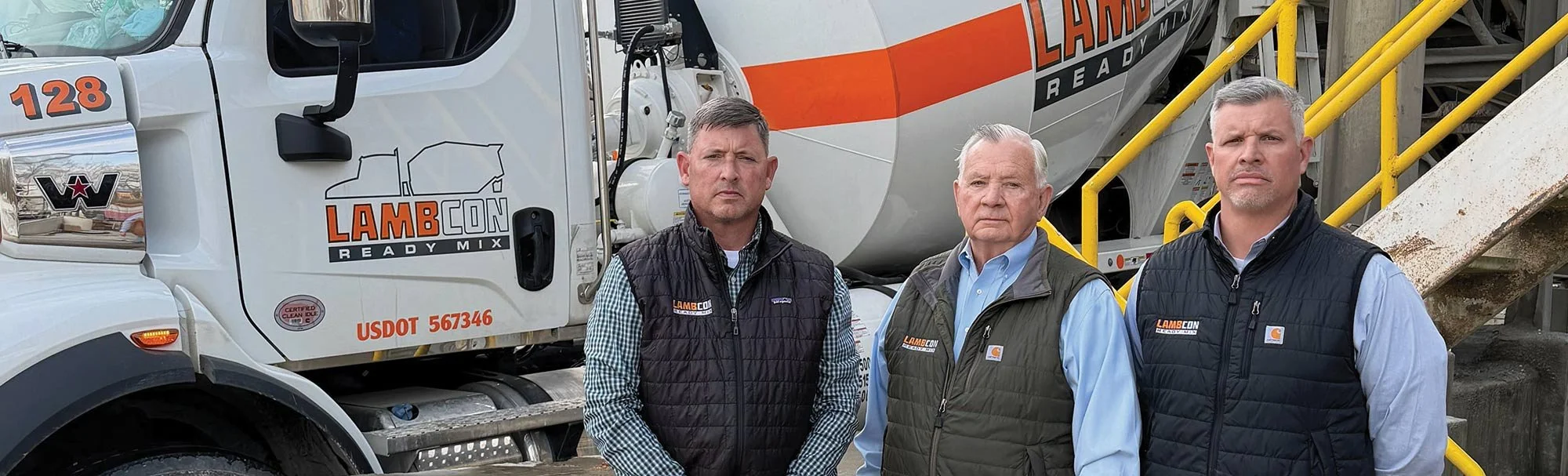 Three men standing in front of a concrete mixing truck with the brand name Lambcon, ladder, and yellow safety rails.