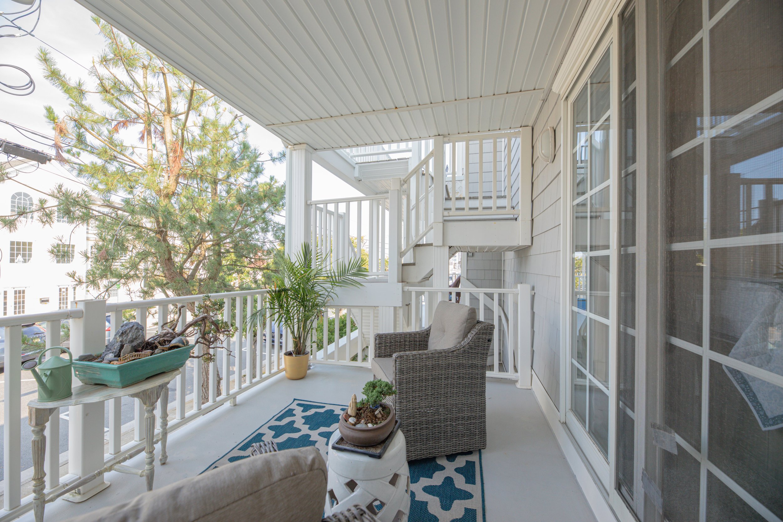 A balcony with outdoor furniture, potted plants, and a view of trees and other buildings in the background.