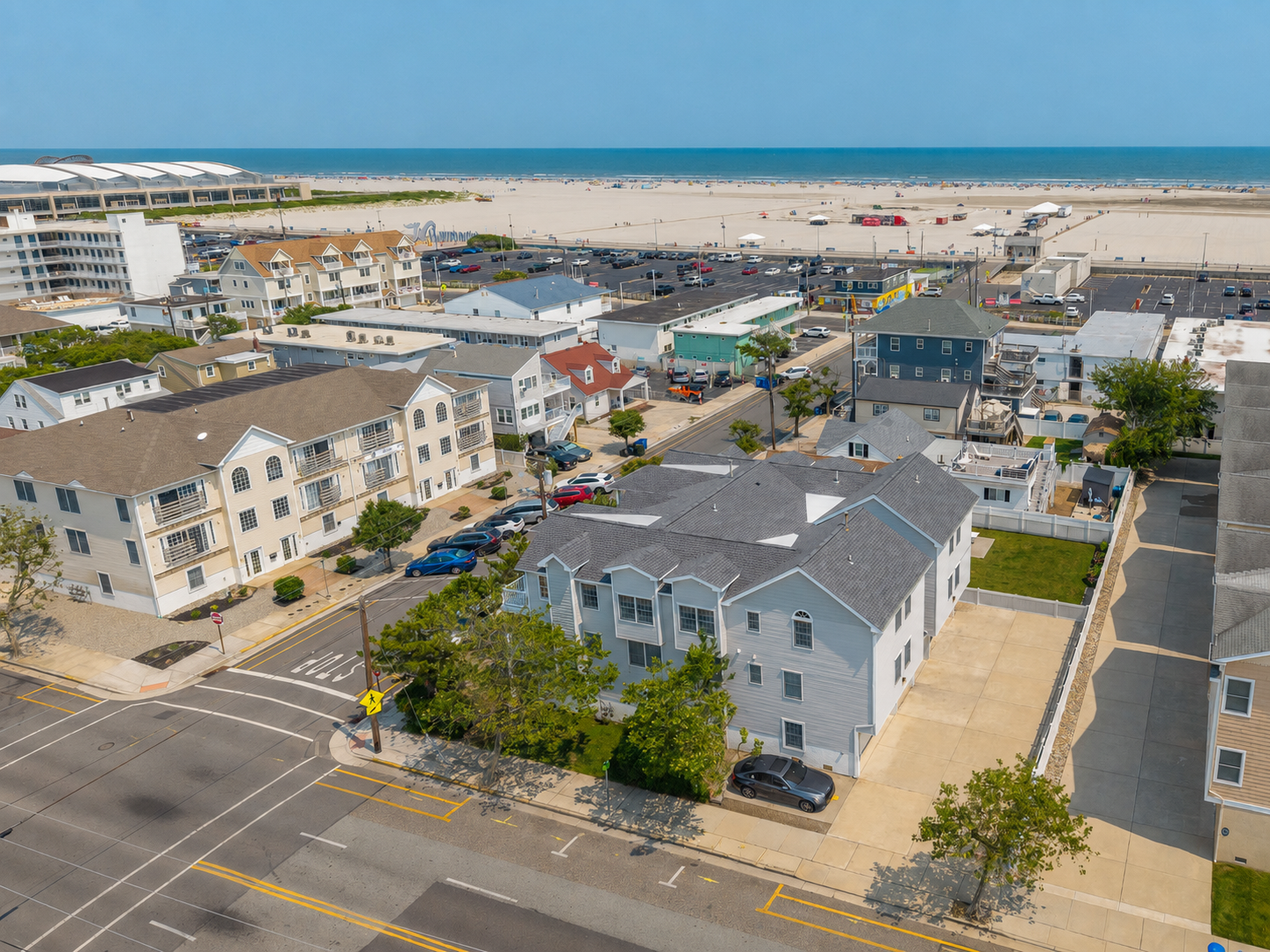 Aerial view of a beachside neighborhood with residential buildings, parking lots, and a sandy beach with the ocean in the background.