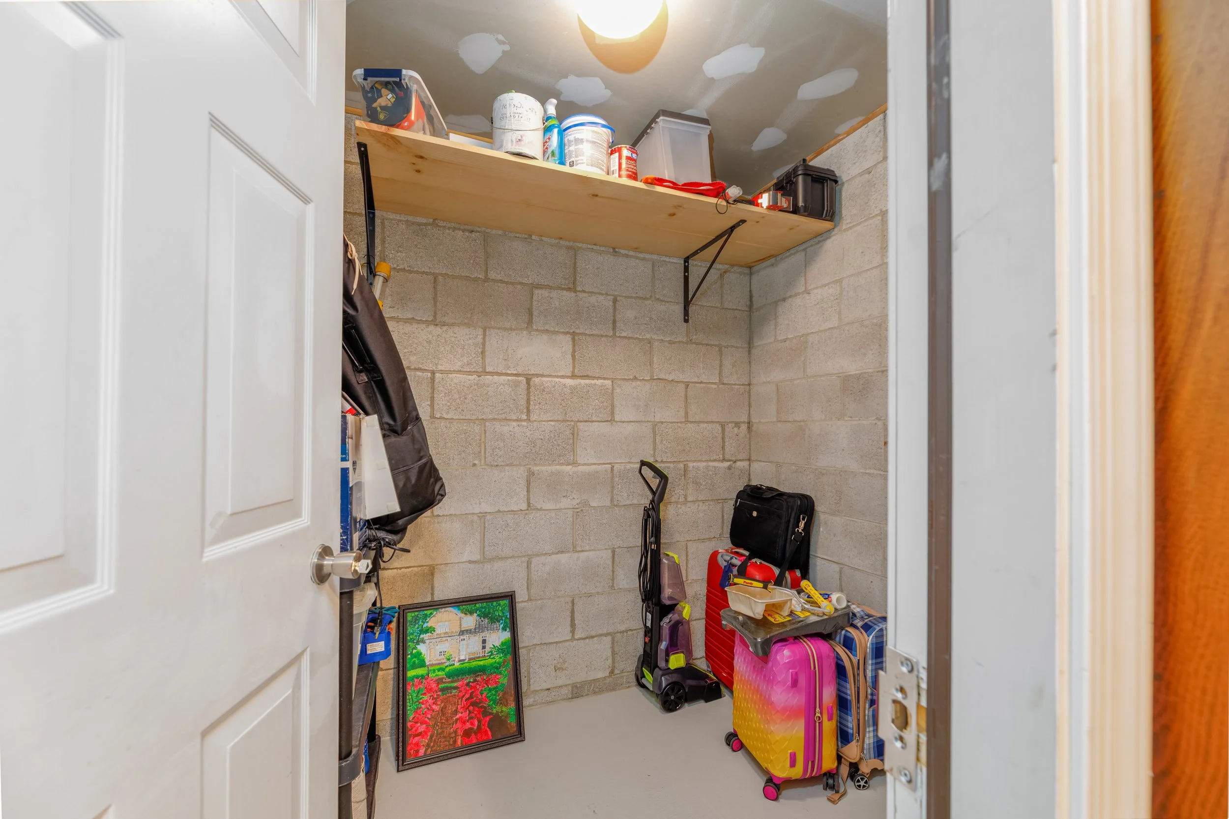 View into a laundry or storage room with various tools, backpacks, and a colorful suitcase against unfinished concrete block walls and decorated ceiling with clouds and a moon mural.