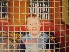 Child smiling behind a red net at an amusement park