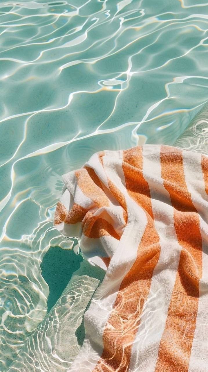 A towel with orange and white stripes floating on a swimming pool with clear water and sunlight reflections.