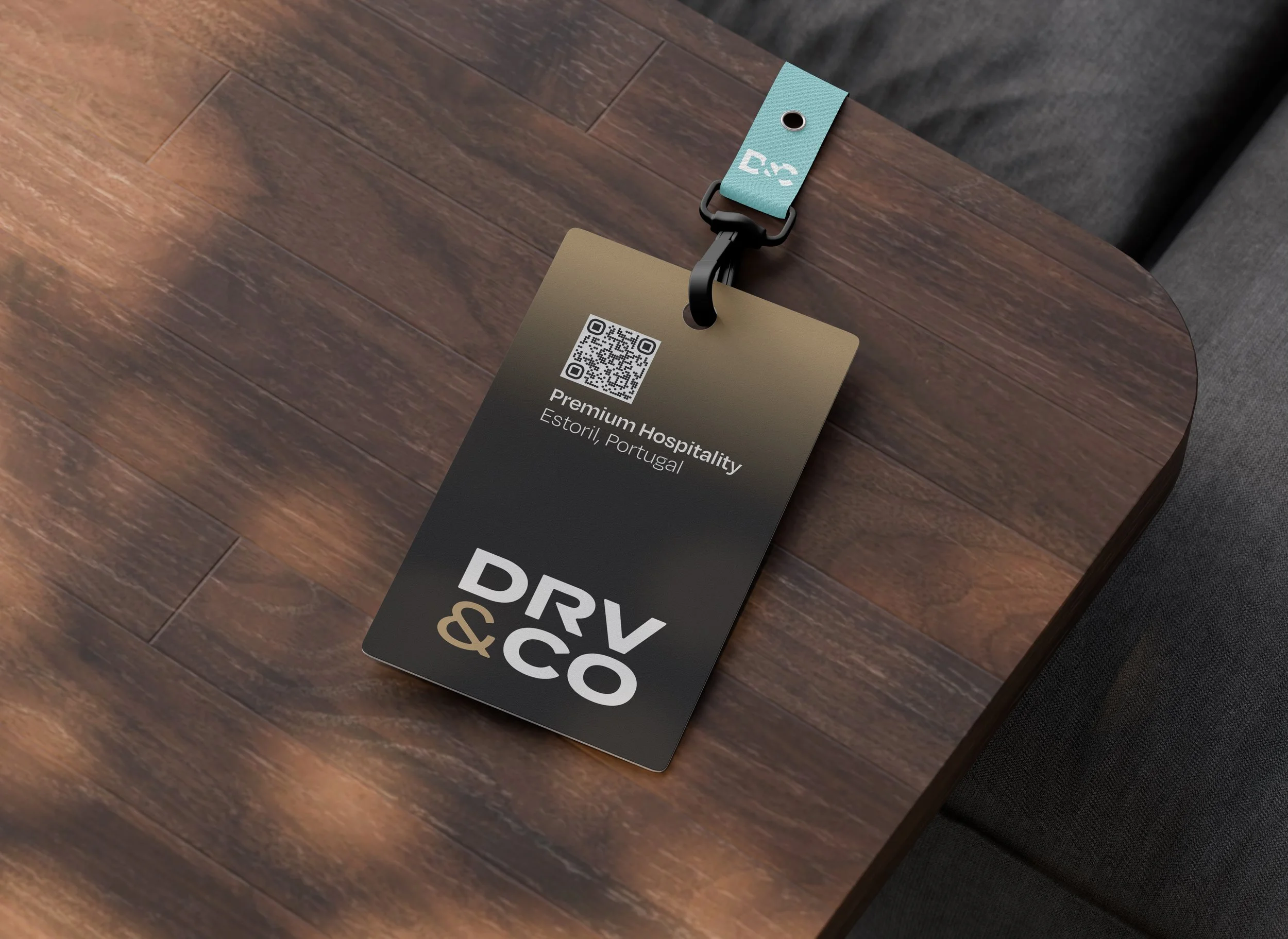 A hotel key card attached to a lanyard, resting on a wooden surface. The key card has a QR code, mentions 'Premium Hospitality' in Estoril, Portugal, and has color accents of teal and black.