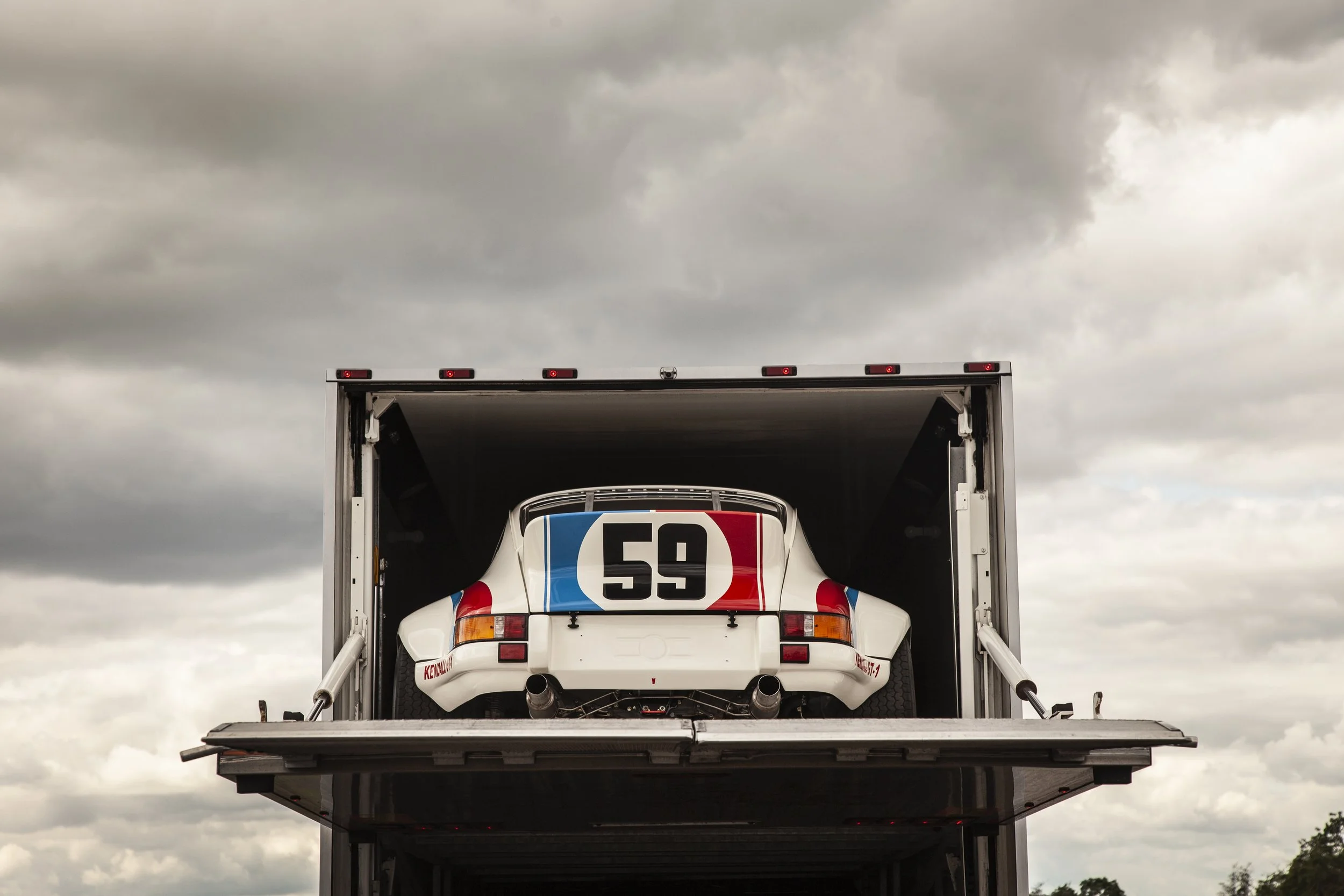 Race car being loaded onto a truck for transport against a cloudy sky.