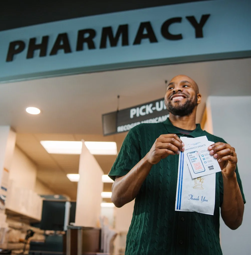 A photo of a smiling man exiting a pharmacy with a prescription in his hands.