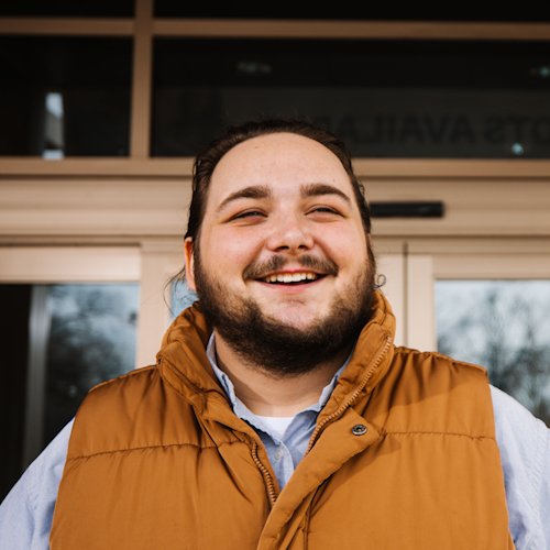 An image of a man in a jacket standing in front of the doors to the Family Health Center, smiling.
