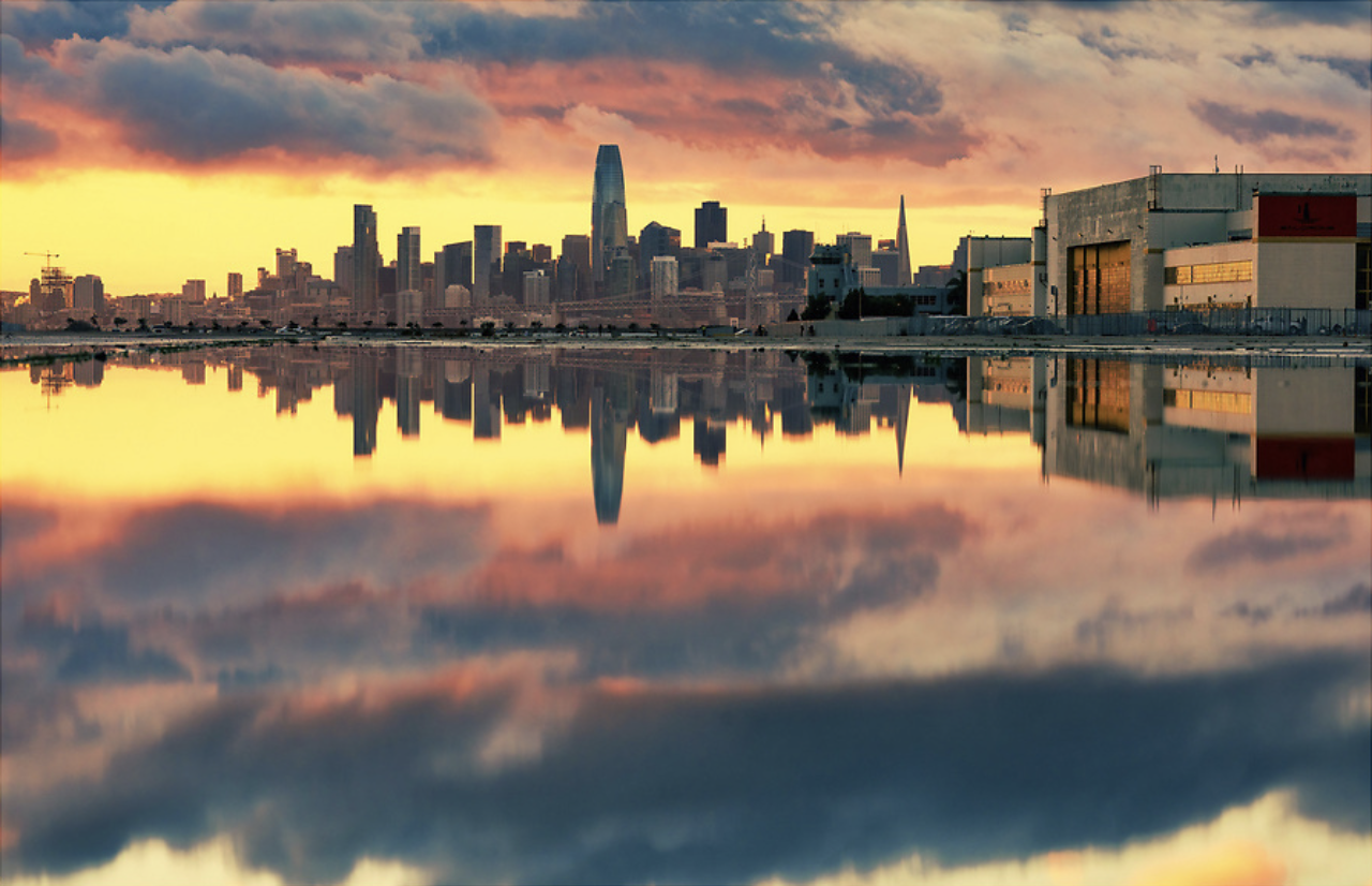 San Francisco skyline at sunset, reflected on water with colorful clouds in the sky.