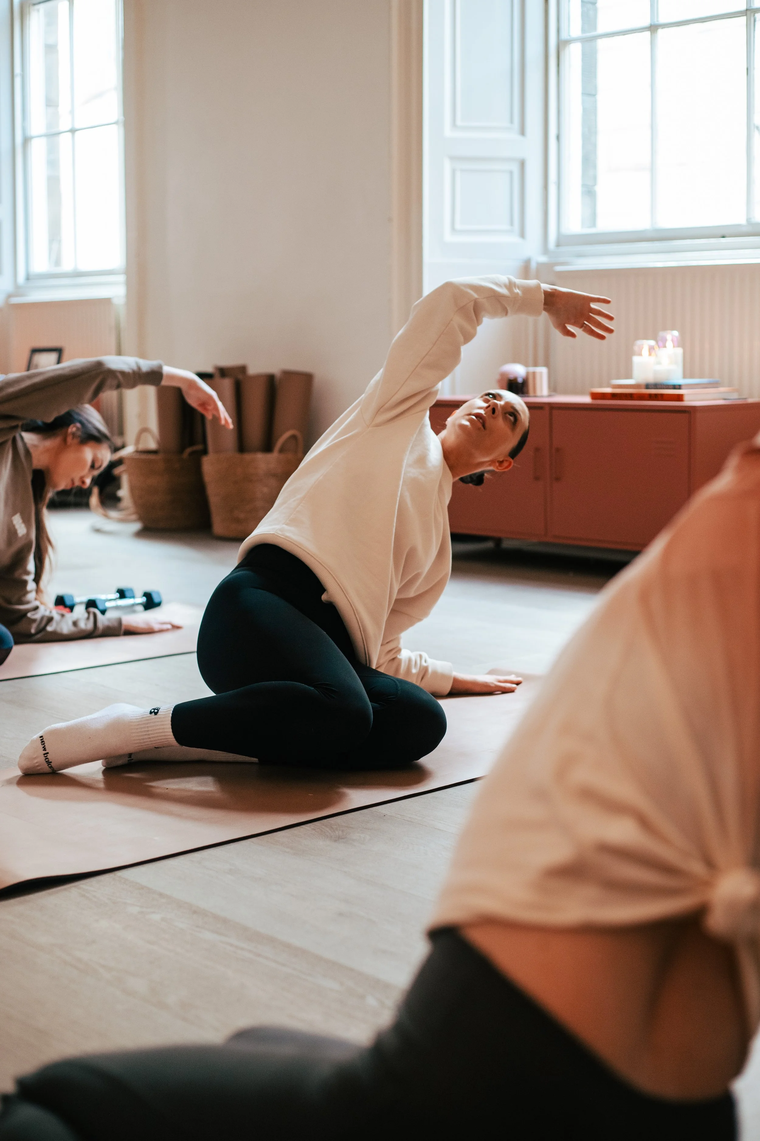 People practicing yoga or stretching on mats in a well-lit room with large windows.