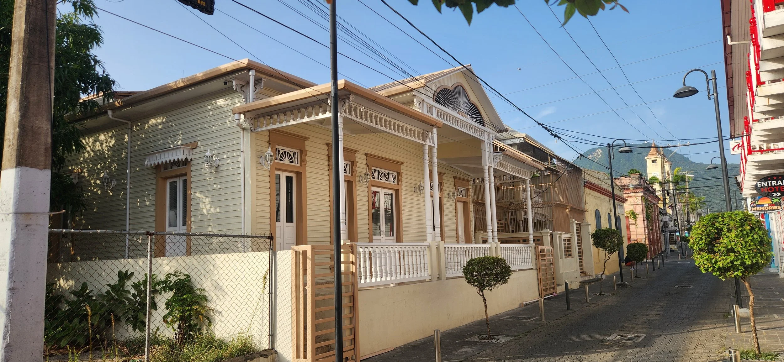 A quiet street with Victorian-style houses, power lines, trees, and mountain in the background on a clear day.