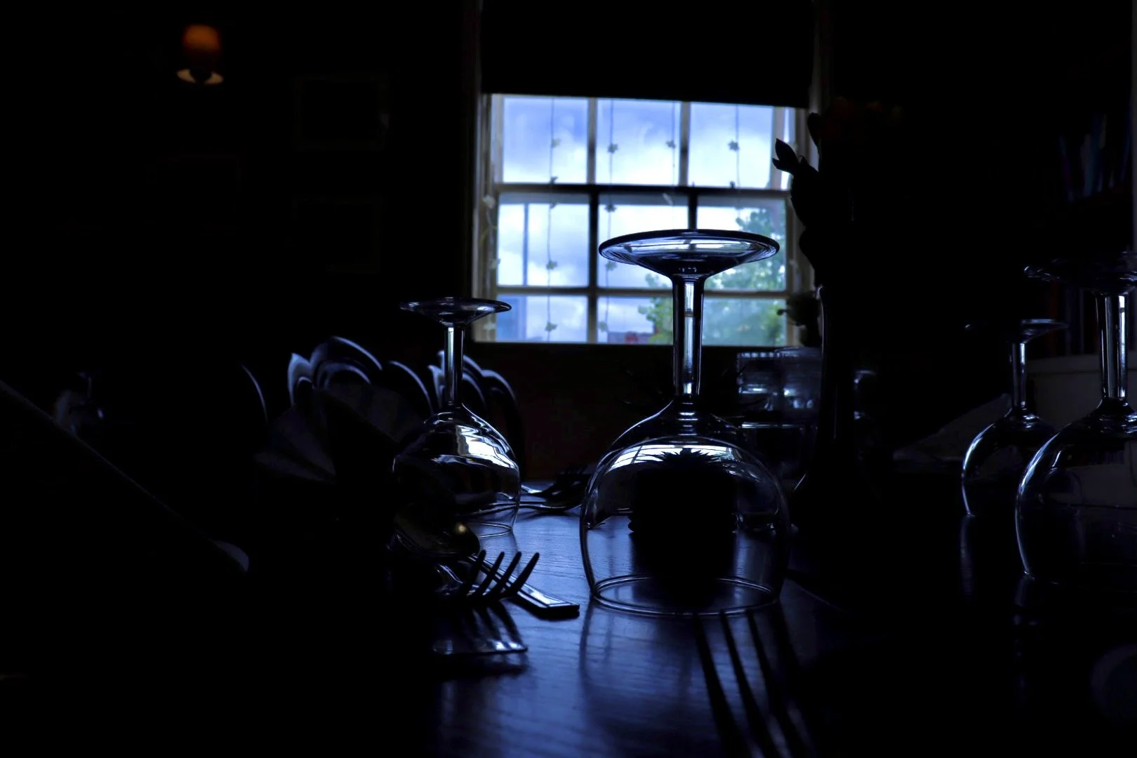 Upside-down wine glasses on a table with a window in the background showing a cloudy sky and trees.