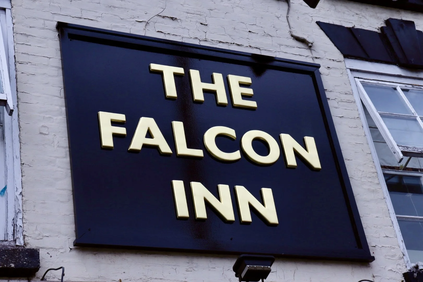 Sign on a brick wall reading 'The Falcon Inn' in cream-colored 3D letters.