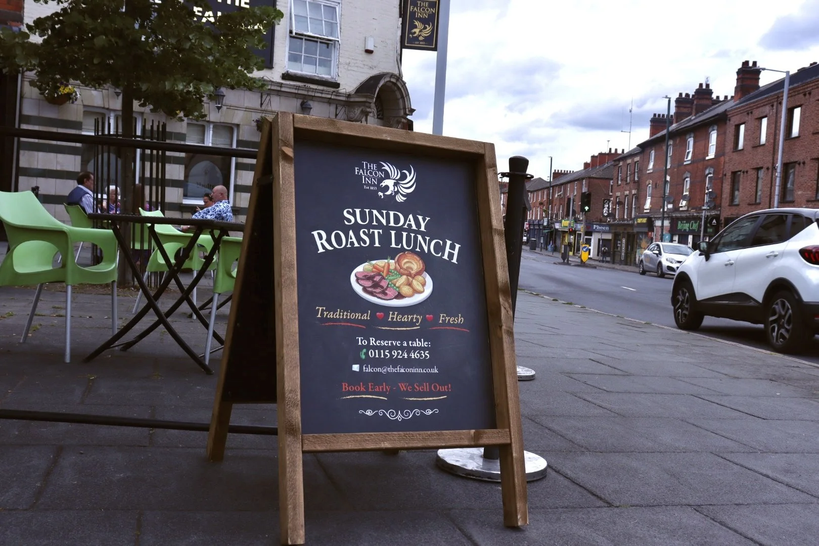 A sidewalk sign advertising a Sunday roast lunch at The Falcon Inn, with a picture of a plate of roast meat and vegetables, and contact information for reservations.
