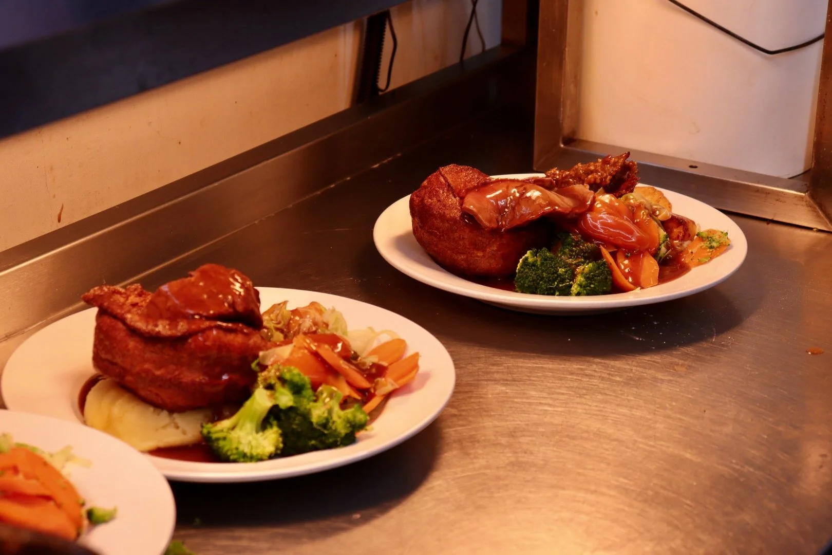 Two plates of Sunday Roasts with gravy, mashed potatoes, broccoli, and mixed vegetables. One roast chicken, one roast beef.