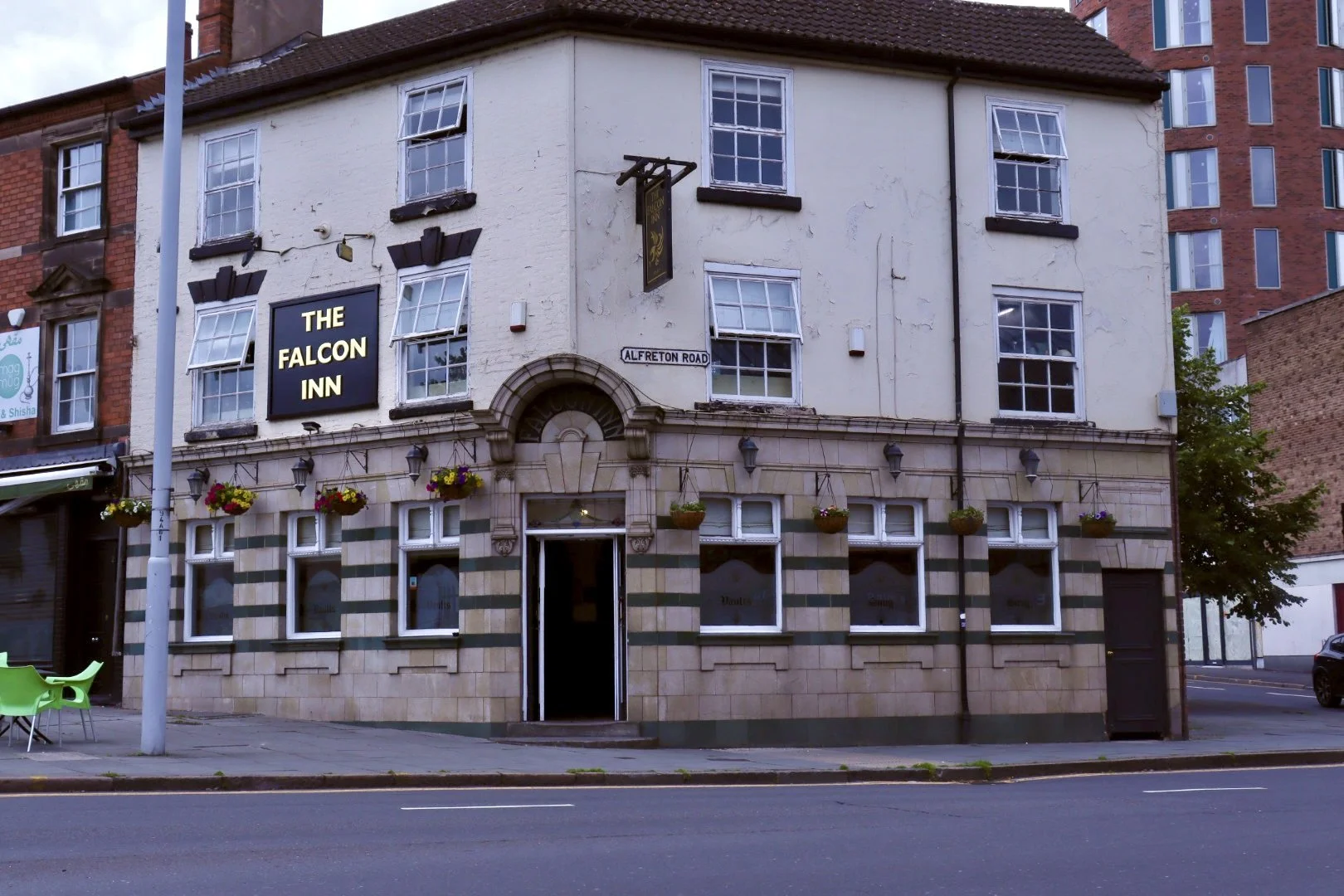 Facade of The Falcon Inn pub on Alfreton Road with hanging flower baskets, signage, and open door, in an urban setting.