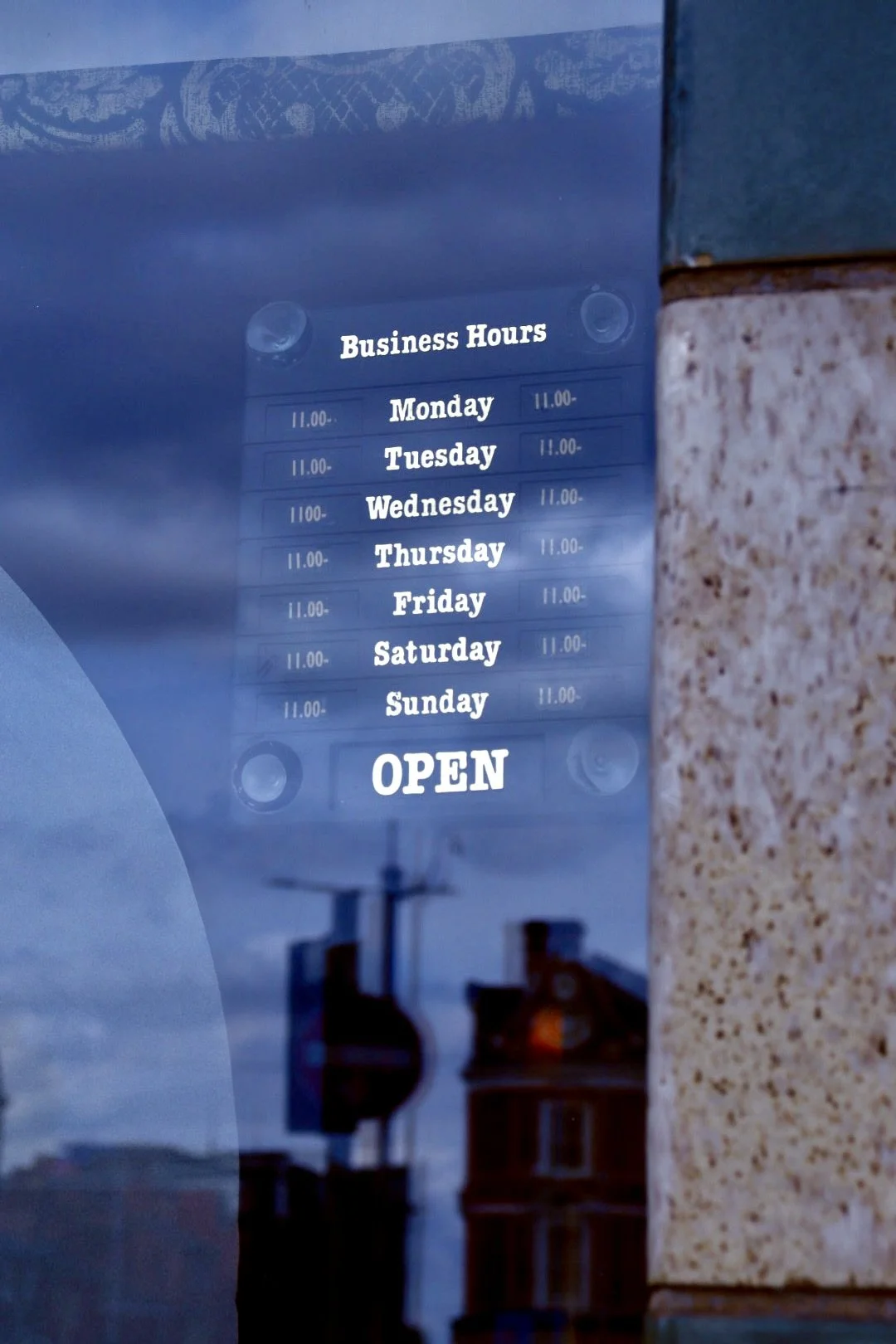 Business hours sign listing operating hours from Monday to Sunday, indicating the business opens at 11:00 AM and is currently open.
