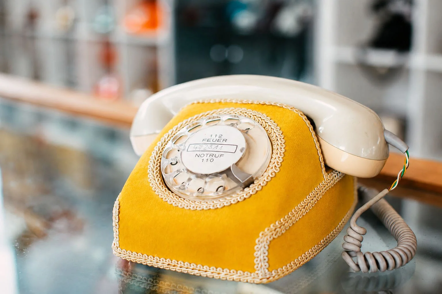 Vintage rotary dial telephone with a yellow fabric cover on a reflective surface.
