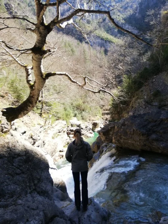 Anna Heinrichs standing beside a mountain stream and waterfall.