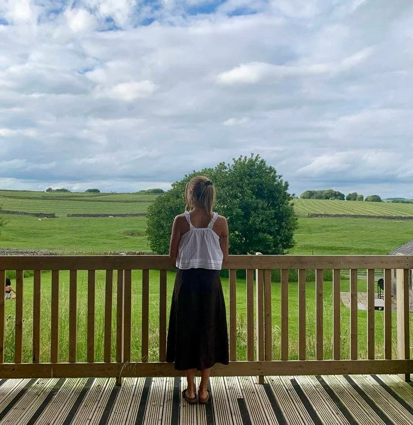 Anna Heinrichs looking across an open green landscape from a wooden balcony.