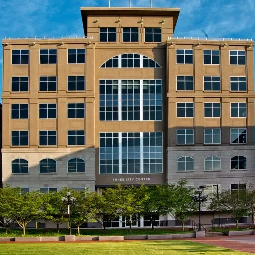 Front view of a multi-story commercial building labeled 'Three City Center' with trees and a park in front.