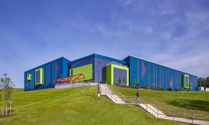 Modern colorful building on a grassy hill with stairs and a person walking nearby.