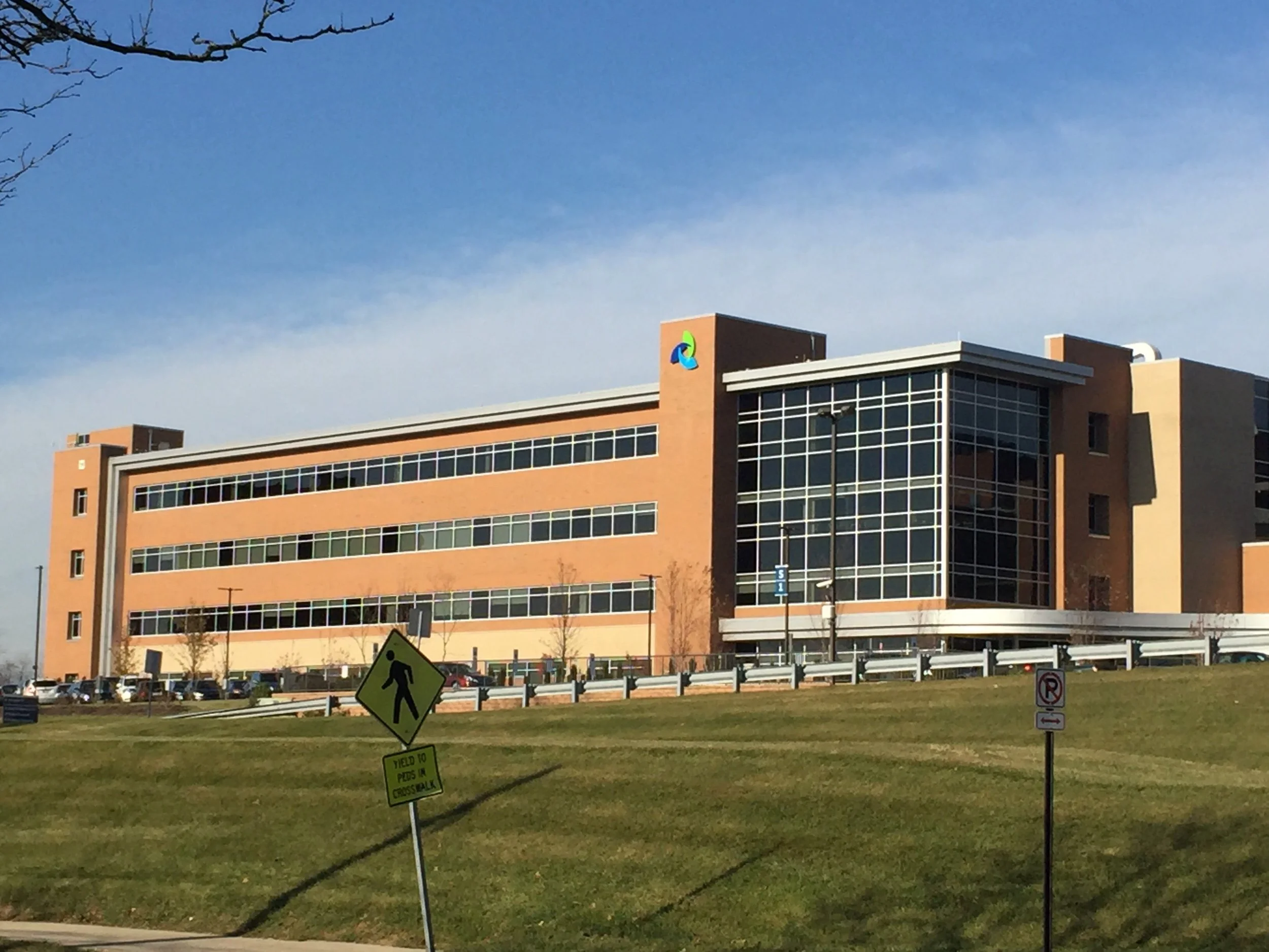 A multi-story office building with a modern design featuring large glass windows and brick walls. There is a colorful logo on the top corner of the building, and the sky is clear with no clouds.