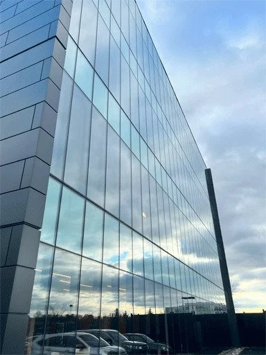 Reflective glass facade of a modern office building under a cloudy sky.
