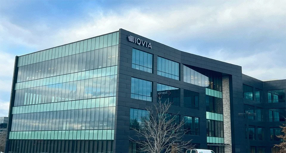 Modern office building with glass facade and the logo 'ELOVIA' at the top, under a cloudy sky.