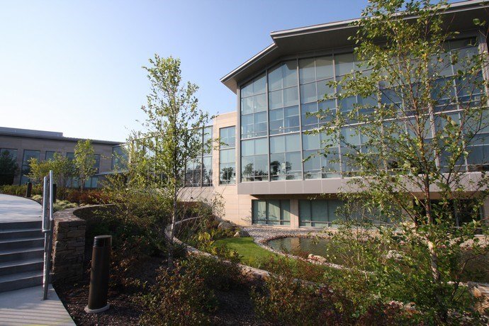 Modern office building with large glass windows, surrounded by greenery and a landscaped garden.