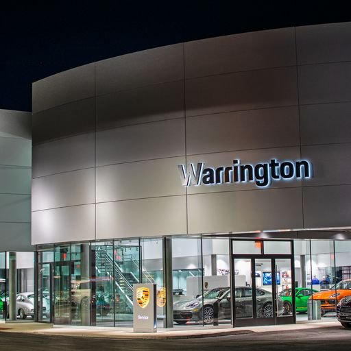Night view of the Warrington Porsche dealership with cars inside and outside, illuminated signage, and glass windows.