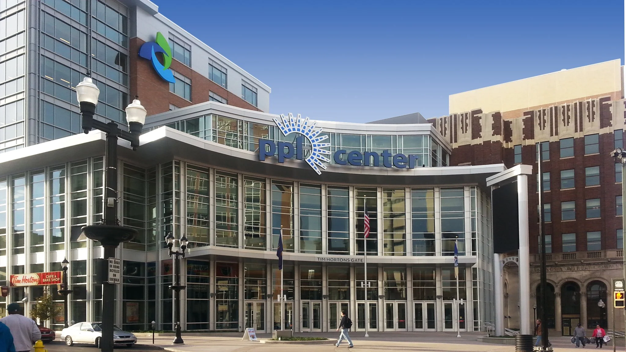 Exterior view of the PPL Center, a modern building with glass windows and signage, in an urban setting with pedestrians and streetlights.