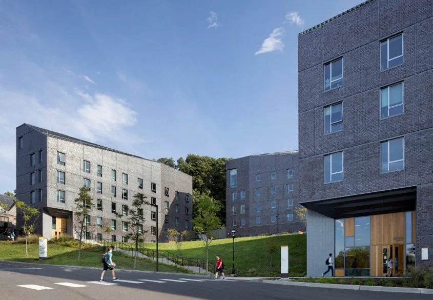 Modern gray apartment buildings on a sunny day with pedestrians walking on the street.