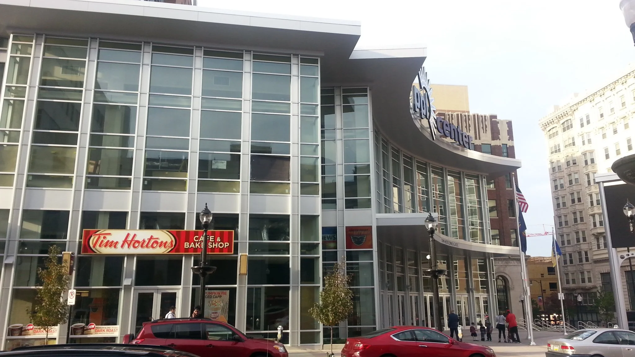 Modern building with large glass windows and a curved facade featuring the ROGR logo. A Tim Hortons coffee shop is on the ground floor, and there are people walking on the sidewalk. Several cars are parked in front of the building.