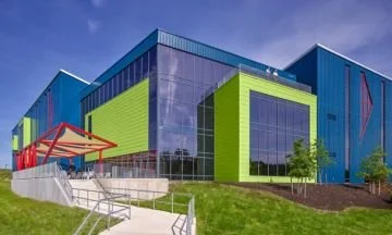 Colorful modern building with large glass windows, green and blue panels, and an orange entrance canopy