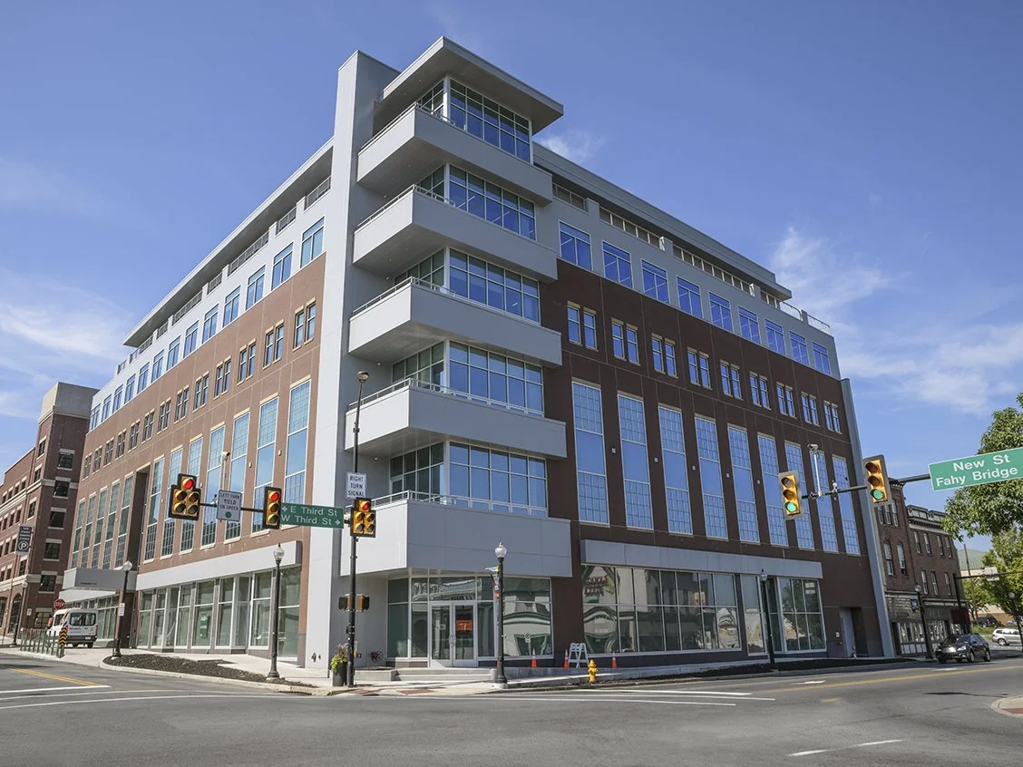 Modern multi-story building with glass windows on a city street corner, traffic lights, and street signs for New Street and Fahy Bridge.
