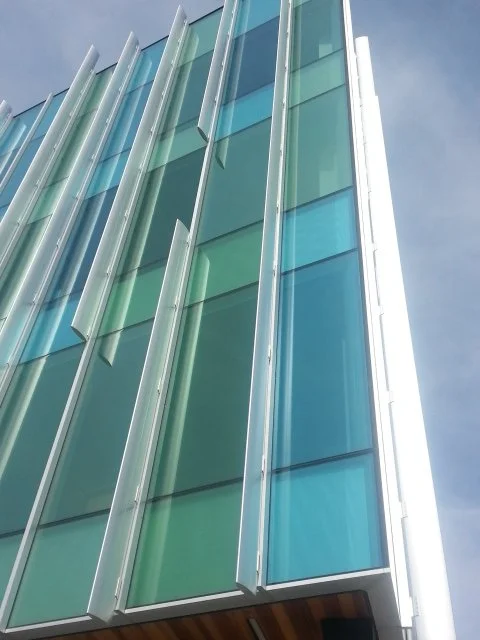 Close-up of a modern glass building facade with angled glass panels and metallic framing.