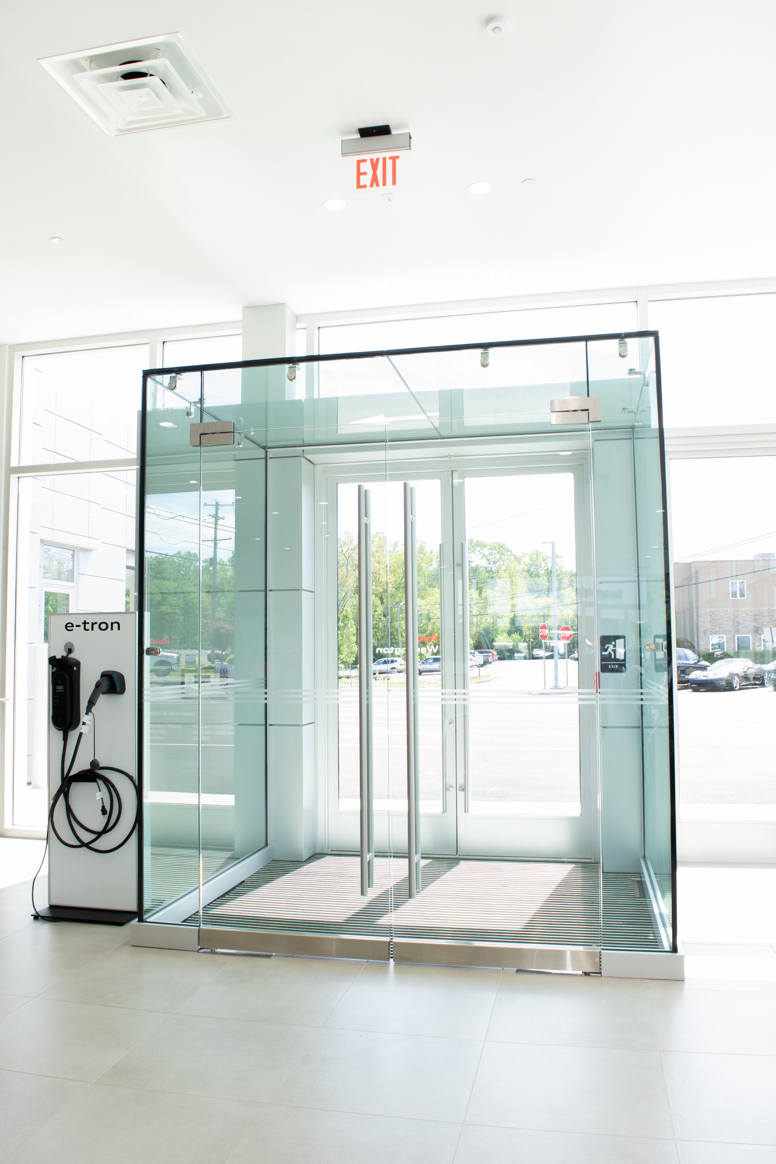Inside view of an electric vehicle charging station near a glass door with exit sign, with electric vehicle chargers labeled 'e-tron' on the side.