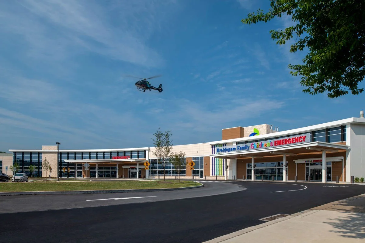 A modern children's emergency and family healthcare center with a helicopter flying overhead on a bright, clear day.