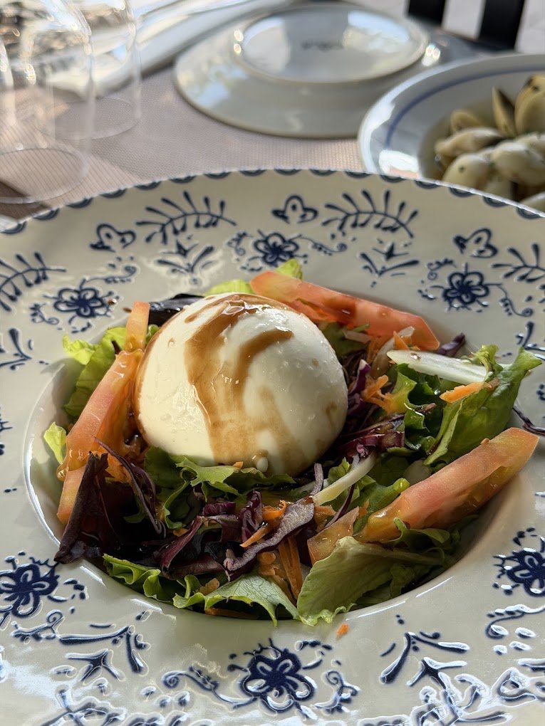 Salad with mixed greens, tomatoes, and a poached egg drizzled with dressing on a decorative plate.