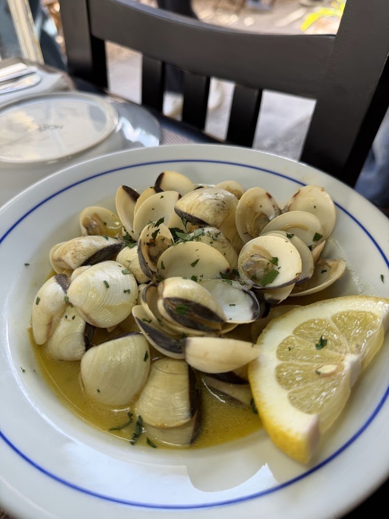 Bowl of cooked clams garnished with parsley and lemon wedges.