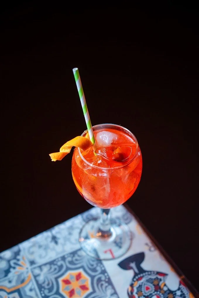 A bright orange cocktail with a striped straw and an orange peel garnish on a decorative napkin.