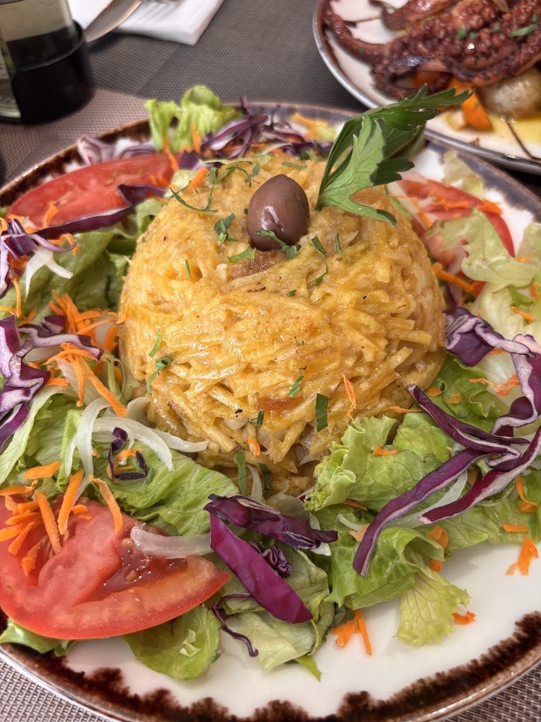 A plate of rice casserole with lettuce, tomato, and shredded carrots, garnished with an olive and parsley.