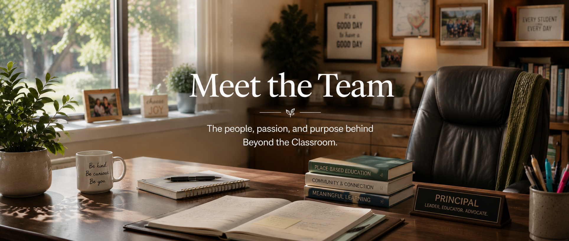 A cozy office or classroom with a large window and a desk. The desk has a potted plant, a coffee mug with inspirational words, a notebook, a pen, and several stacked books labeled 'Place-Based Education,' 'Community & Connection,' 'Meaningful Learning.' There is also an open notebook with handwritten notes. The background features framed photos, a lamp, and shelves with books and decorations. Overlaid text reads 'Meet the Team' and 'The people, passion, and purpose behind Beyond the Classroom.'