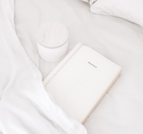 A white notebook with the year '2020' on the cover, a white candle, and a white bedding surface.
