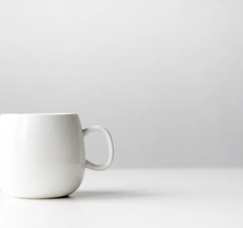 A white ceramic mug on a white surface with a plain white background.