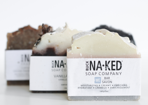 Three bars of Buck Naked soap in vanilla, coconut, and black soap scents with minimal packaging.