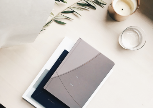 Two notebooks, a candle, a glass of water, and a small plant on a light-colored surface.