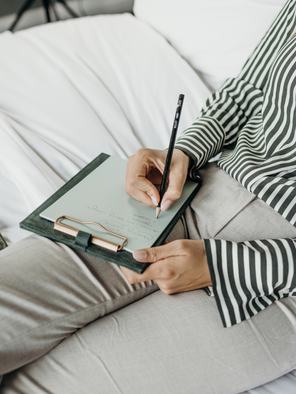 Person sitting on a bed, writing on a clipboard with a notebook attached.
