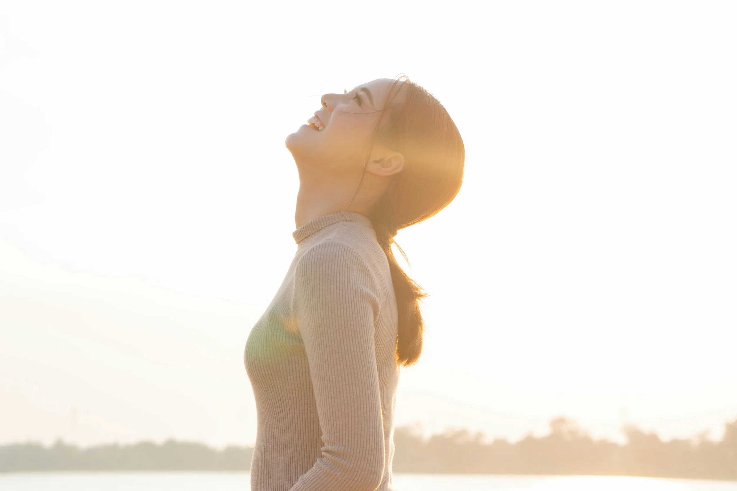 A woman with red hair smiling and looking upward outdoors during sunset or sunrise.