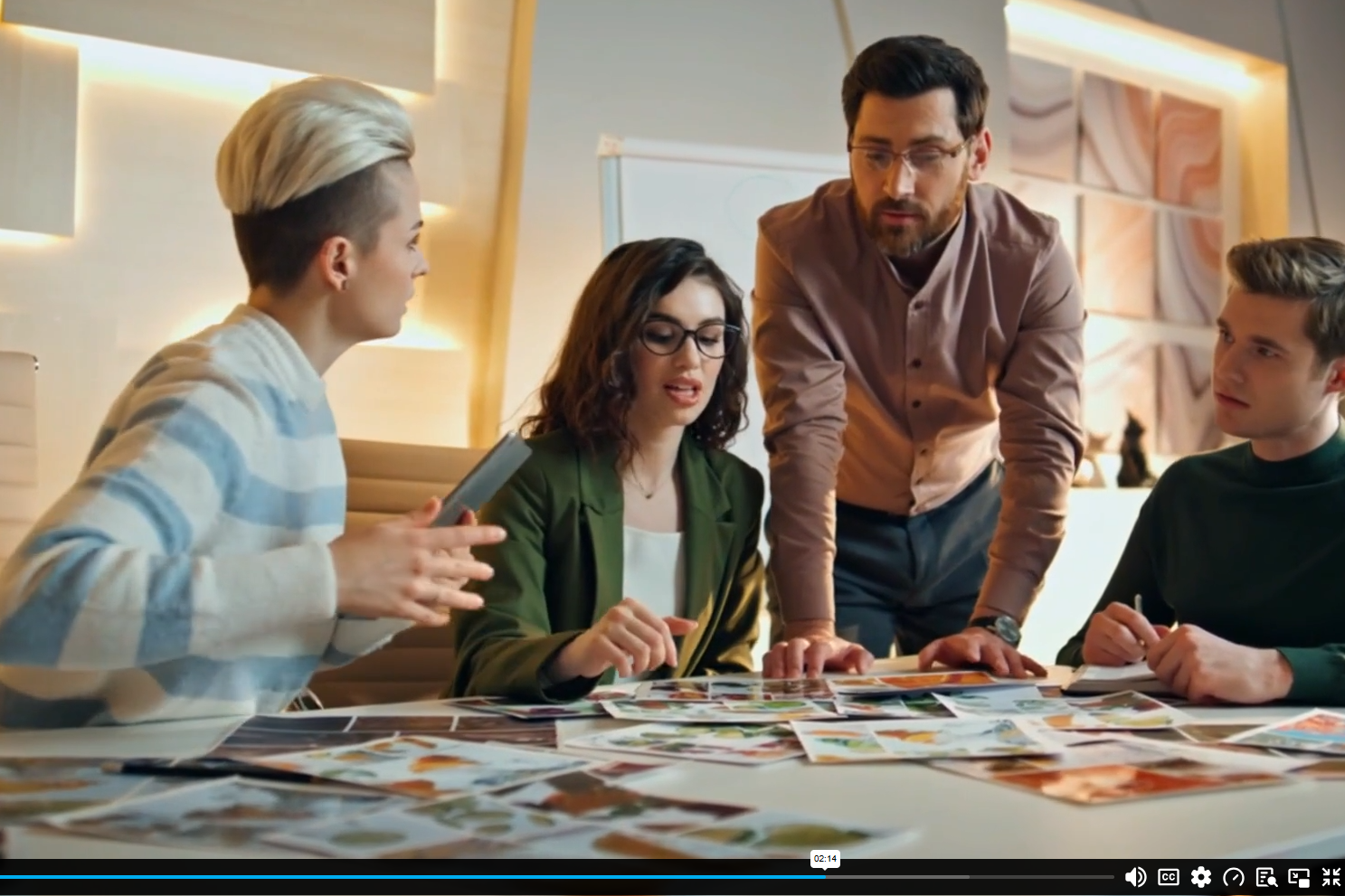Group of four people at a table discussing and analyzing photographs or artwork in a well-lit room.