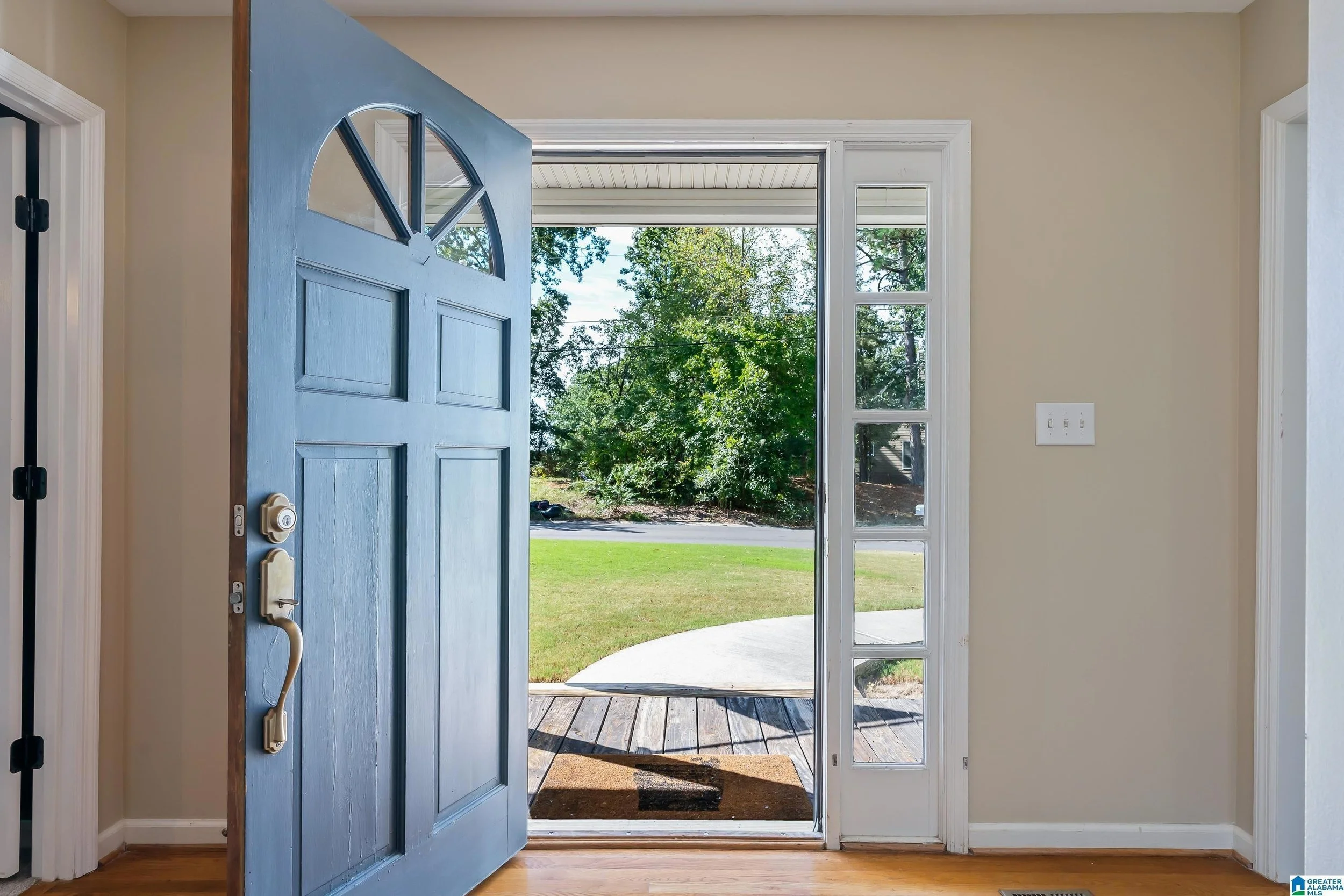 Open front door revealing a porch and grassy yard with trees.